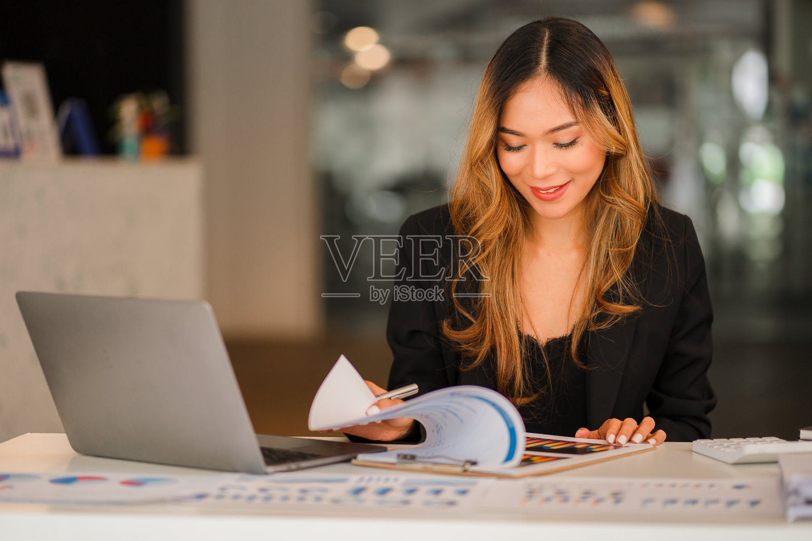 亚洲女商人用文件和笔记本电脑在图表和图表上工作，显示办公室的结果，工人文件计算财务指标，微笑着，为成功而高兴。照片摄影图片