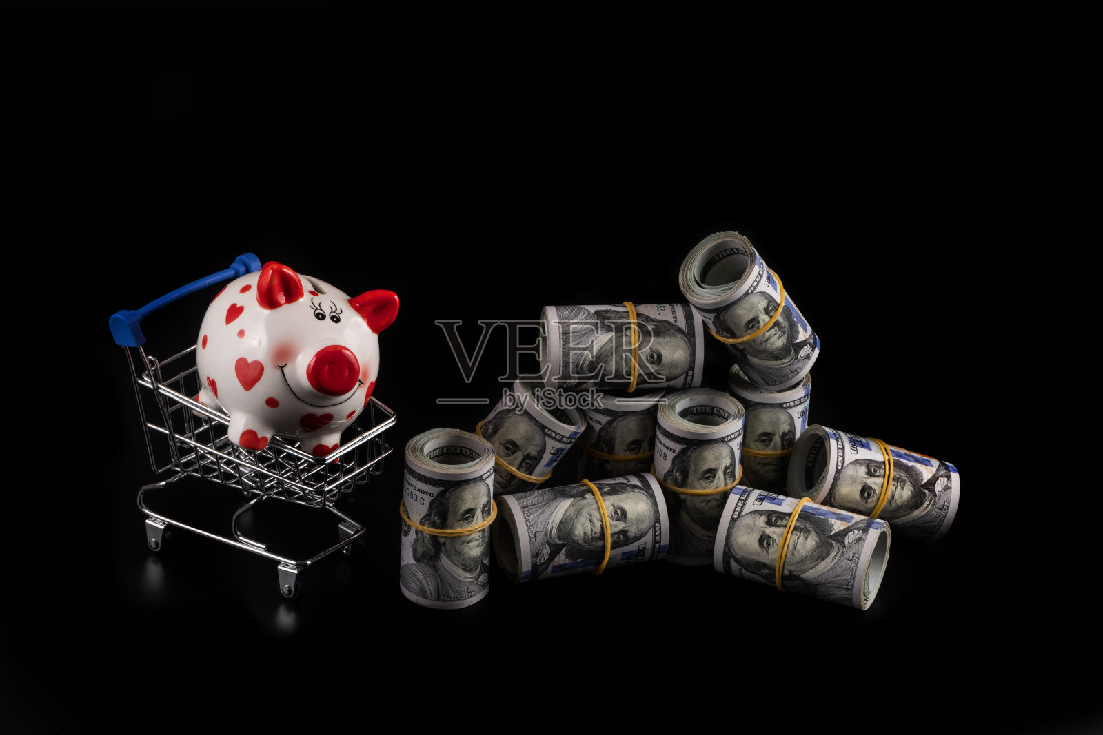 超市里的迷你购物车里有一个存钱罐，黑色背景上有一包美元照片摄影图片