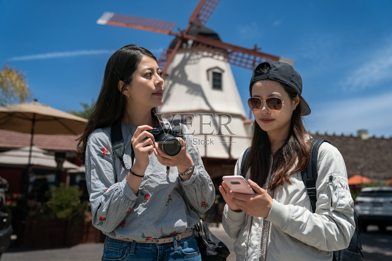 一名亚洲日本妇女好奇地环顾四周，试图用相机捕捉索尔旺的美丽，而她的朋友正在用电话问路，背景是丹麦风车照片摄影图片