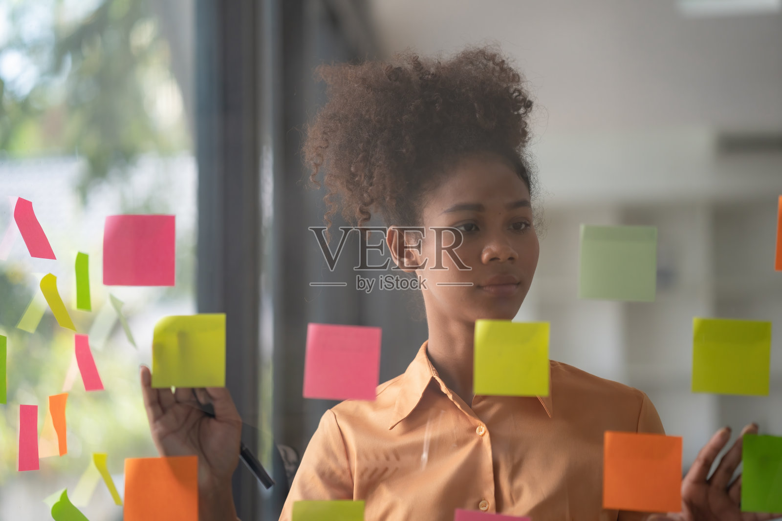 非裔美国商业女性使用贴在玻璃墙上的便利贴来书写战略商业计划，以发展和成长为成功。照片摄影图片