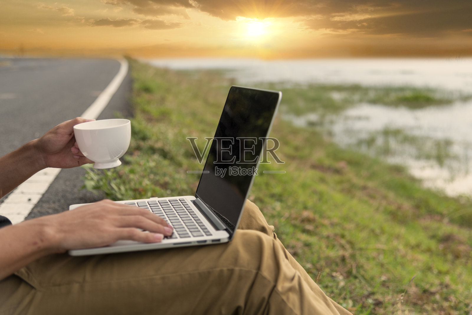 一名男子在办公室外拿着咖啡杯，手里拿着打字笔记本电脑。近距离的男子双手使用电脑笔记本电脑坐在绿色公园户外生活方式。男性使用笔记本电脑家庭办公技术照片摄影图片