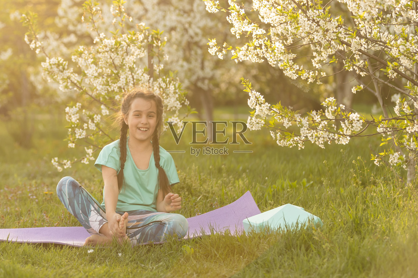 穿着t恤的小女孩在花园里的垫子上做瑜伽。孩子和健康的生活方式照片摄影图片