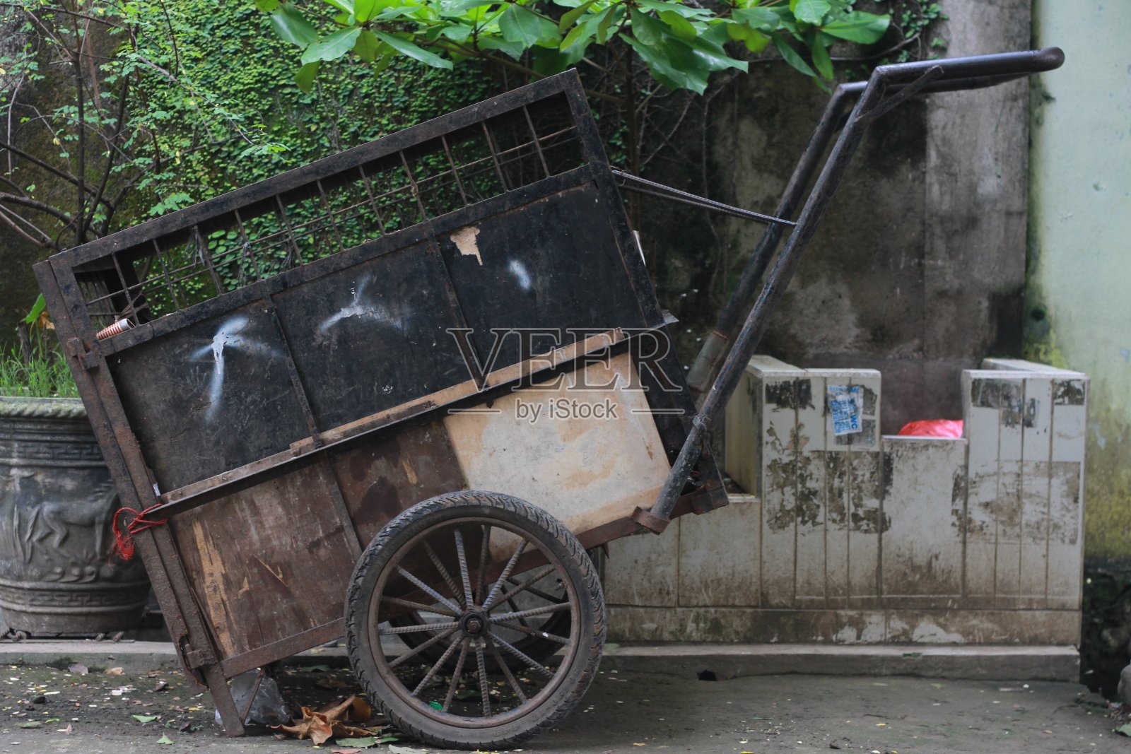 一辆垃圾车停在垃圾桶附近，背景是一堵墙和绿色植物照片摄影图片