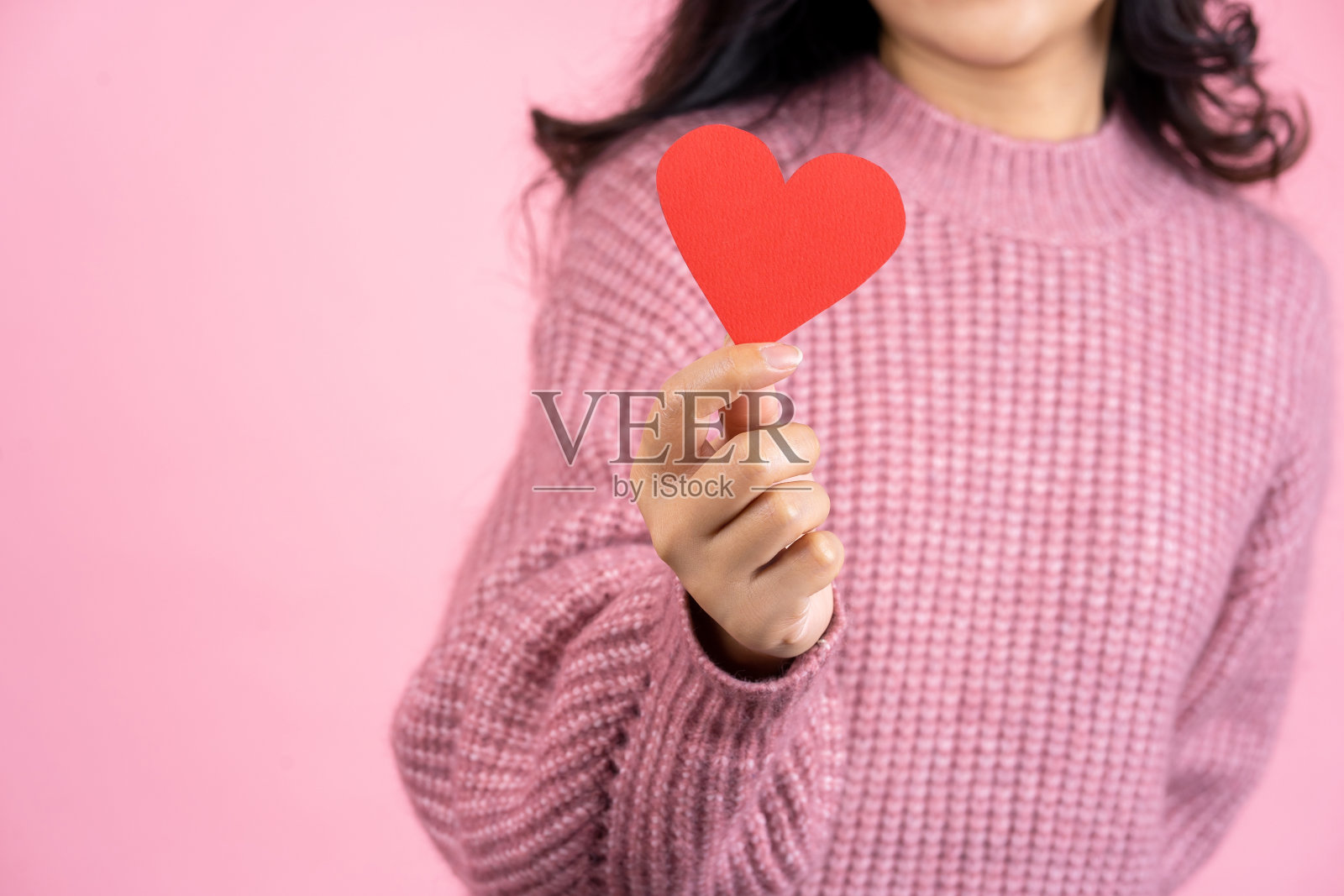 特写镜头的女性手，美丽的亚洲女人穿着粉红色的毛衣是抱着红色的爱的心孤立地站在粉红色的背景，爱的概念照片摄影图片