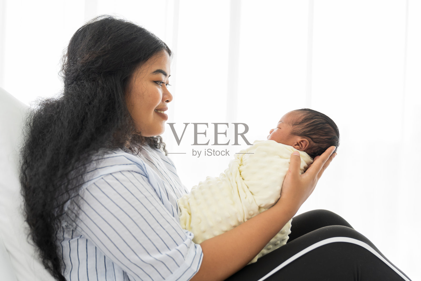 快乐的母亲抱着刚出生的婴儿躺在床上。在医院照顾新生儿的年轻母亲或护士照片摄影图片