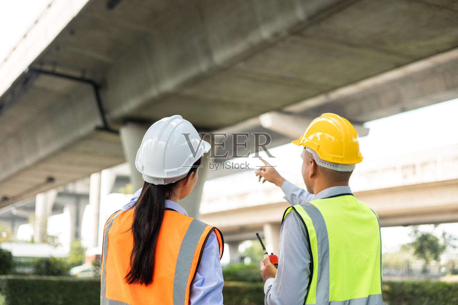 两名亚洲工人工程师和一名女建筑师在工地上戴着白色安全帽看建筑。站在高速公路混凝土路面现场。有蓝图和平板的工作计划。照片摄影图片