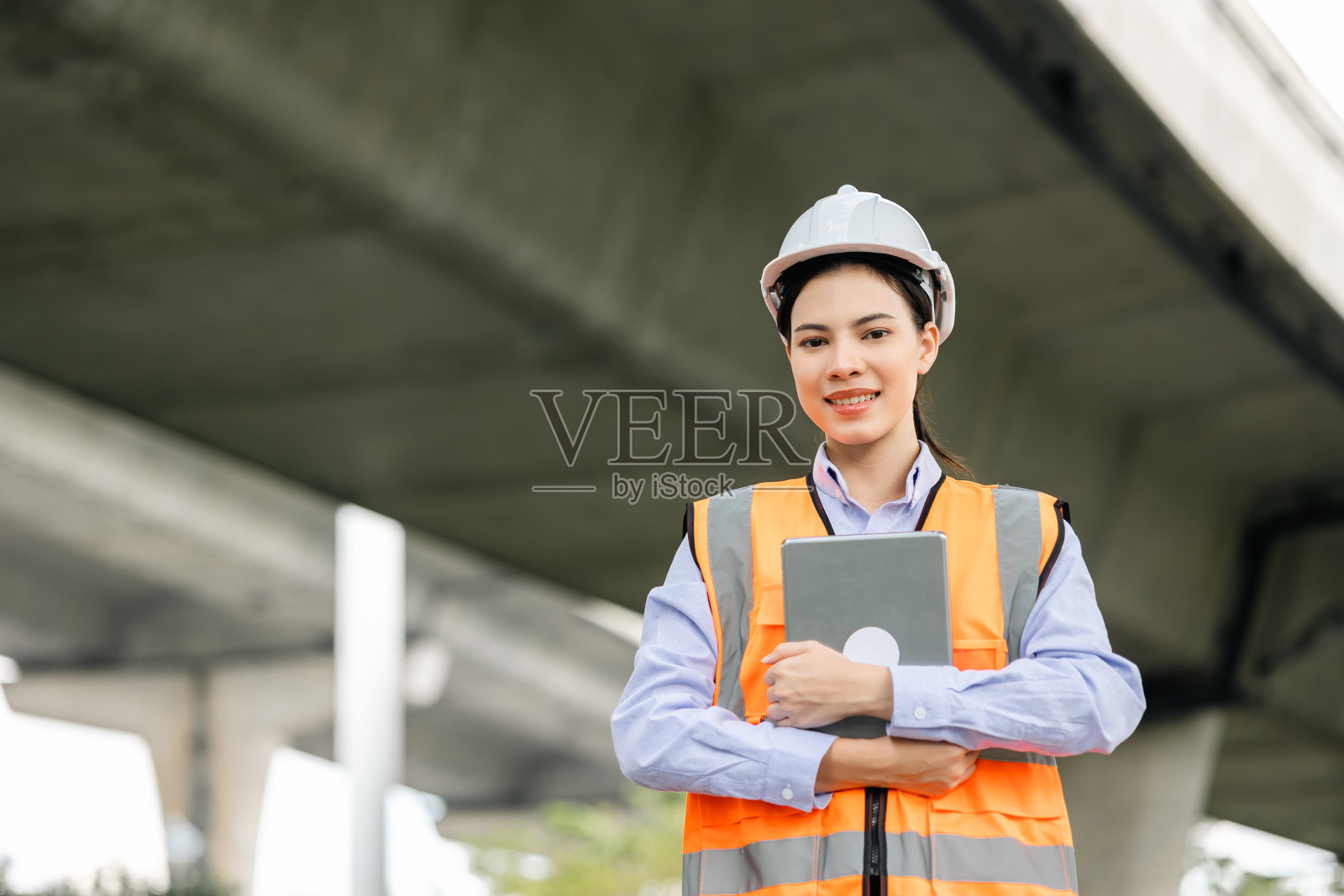 亚裔女工程师、女工人或建筑师在工地上戴白色安全帽。站在高速公路混凝土路面现场。公路桥进度规划。照片摄影图片