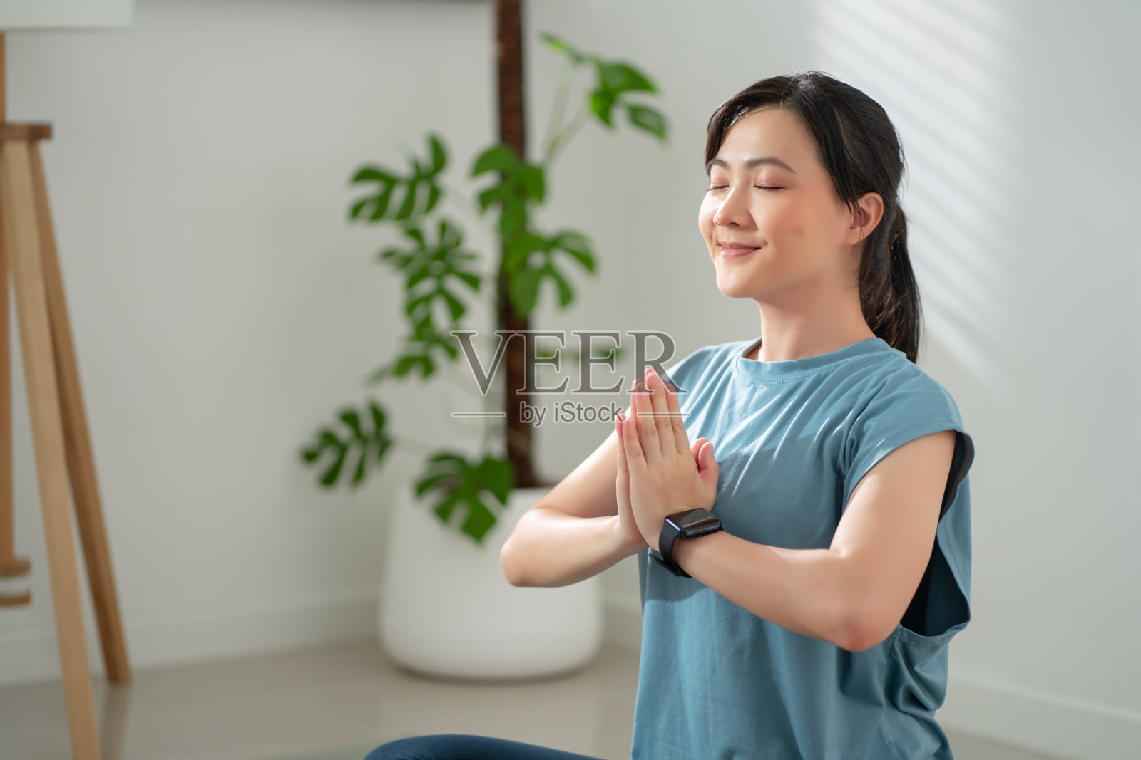 亚洲妇女在垫子上练习瑜伽闭着眼睛在家里的客厅冥想。照片摄影图片