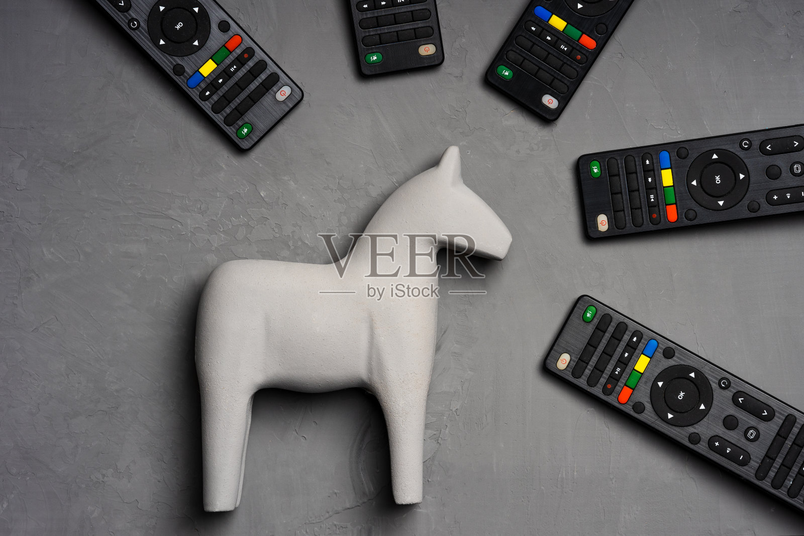 灰色背景的灰色玩具马，电视遥控器围绕着它照片摄影图片