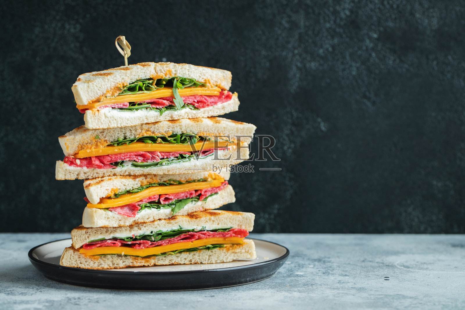 自制的大三明治，有香肠、奶酪和芝麻菜，背景是深色混凝土照片摄影图片