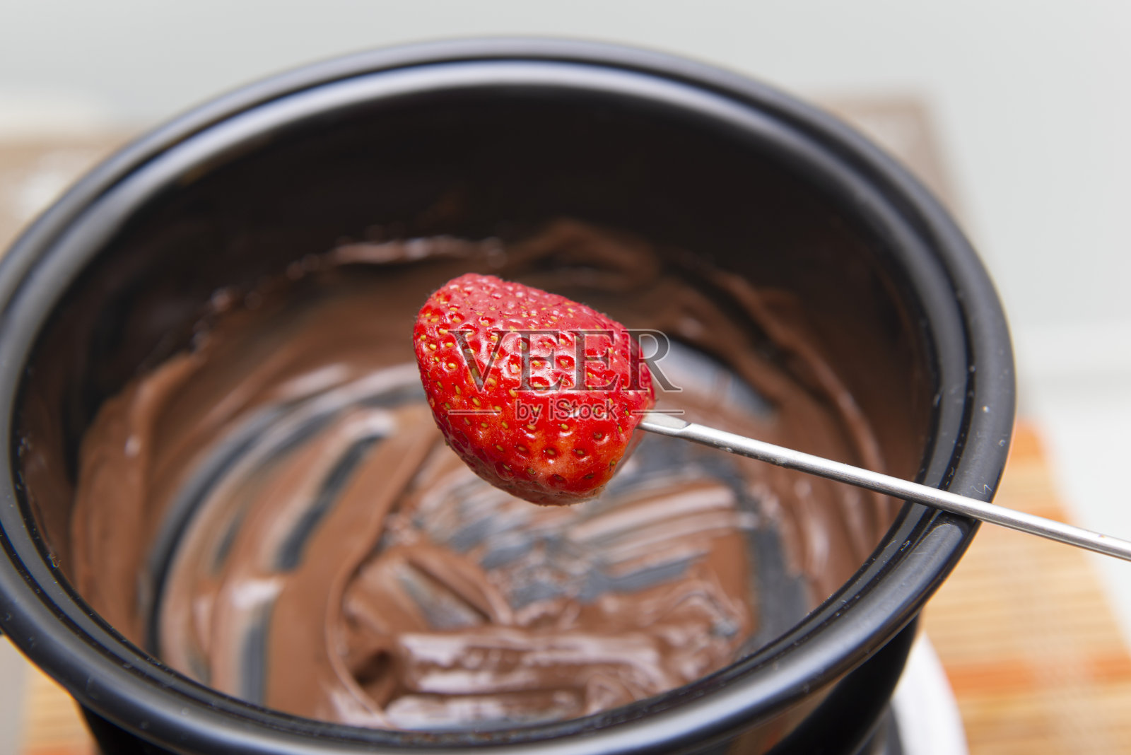 一个人用草莓蘸巧克力火锅。照片摄影图片