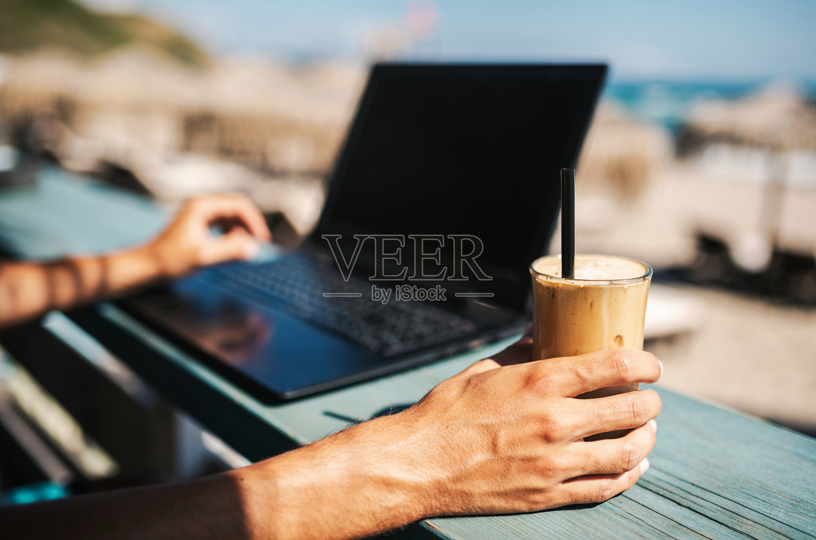 一个不认识的男人在海滩上一边工作一边喝冰沙咖啡照片摄影图片