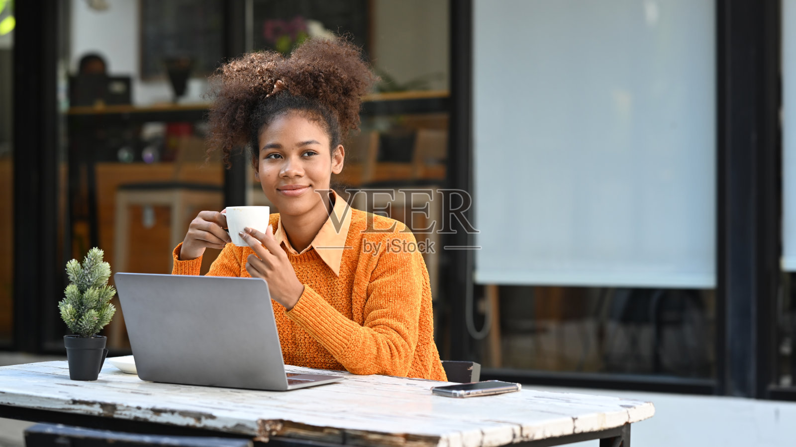 迷人的年轻女性自由职业者喝咖啡和使用笔记本电脑在户外咖啡馆。照片摄影图片