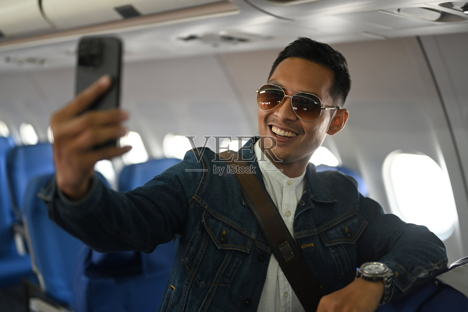 自信的亚洲男性旅行博主靠在飞机座位上，拿着相机录制他的视频博客。照片摄影图片
