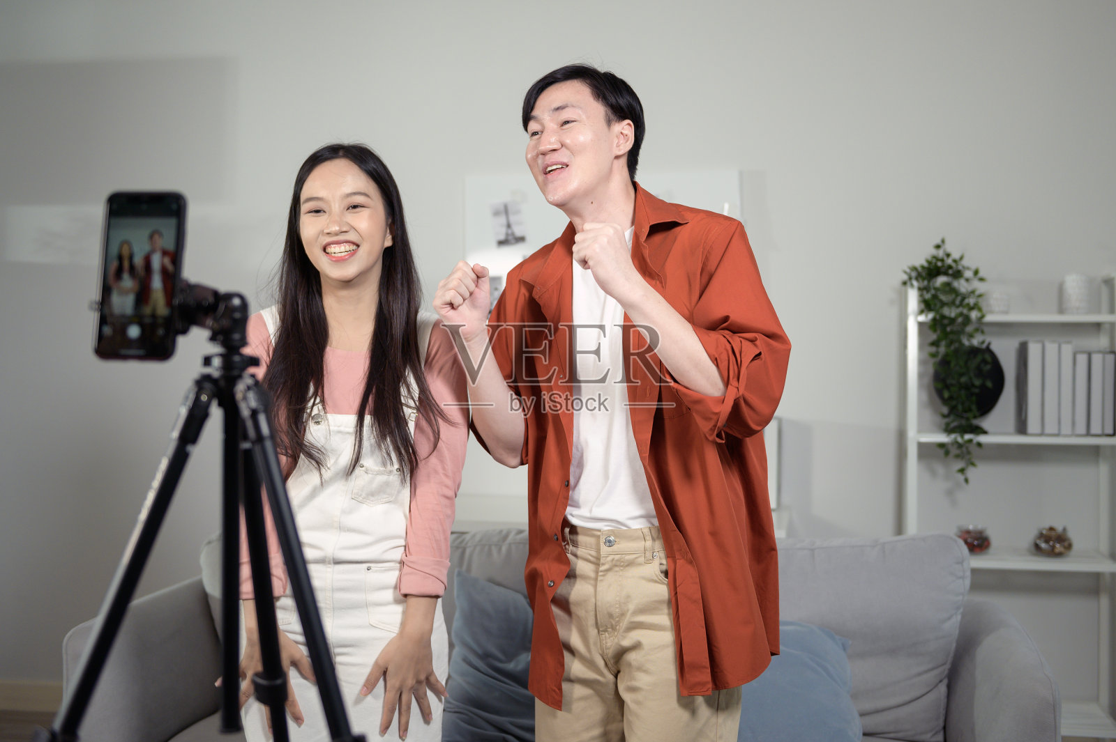 亚洲的年轻情侣们正在一起用智能手机制作舞蹈视频，并在社交媒体上分享视频内容。照片摄影图片
