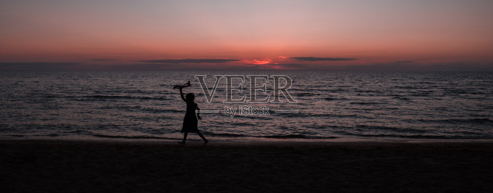 日落时分，快乐的女孩带着风筝在户外奔跑。日落时分，一个孩子在大海的背景下拿着风筝奔跑。家庭度假。照片摄影图片