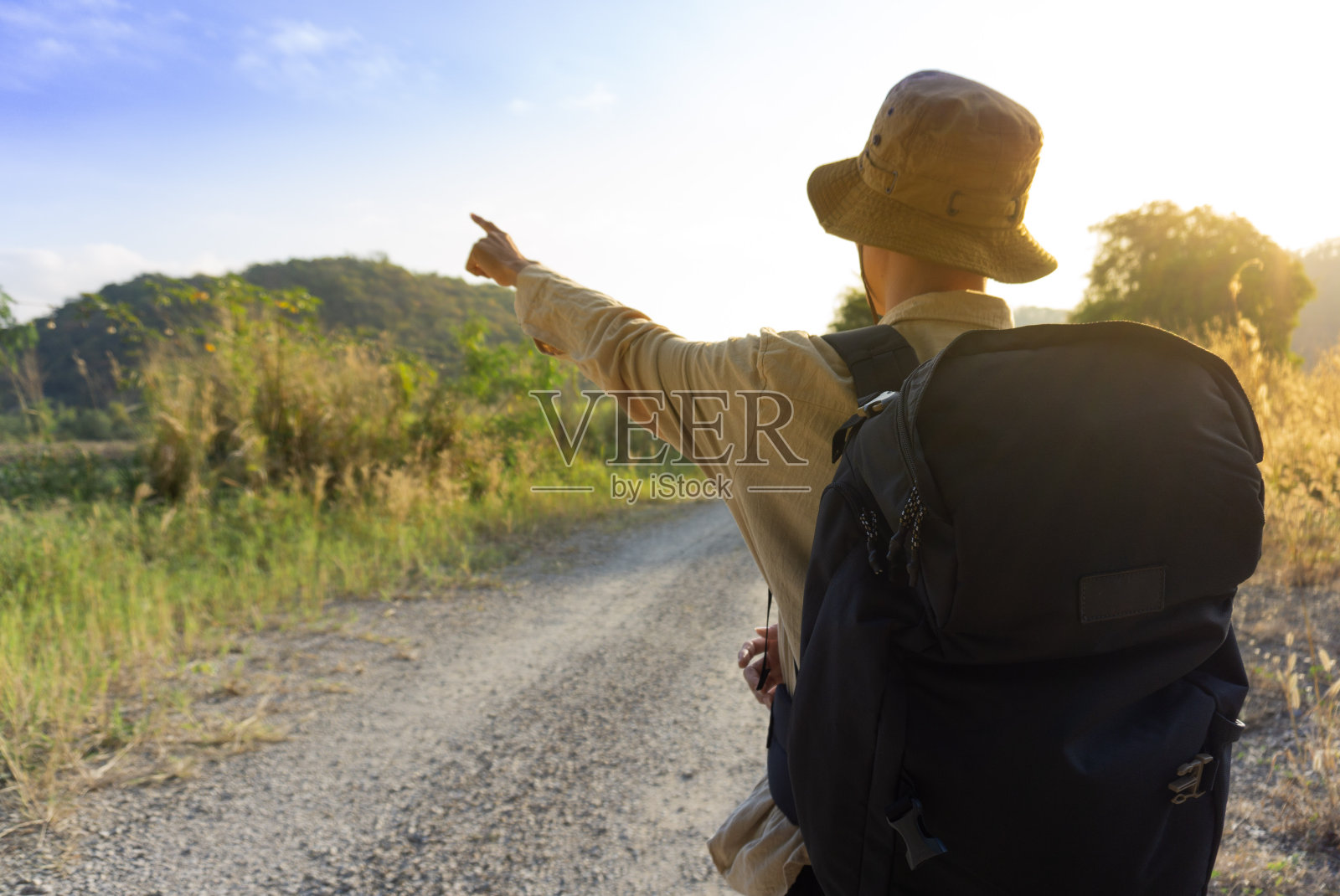 一个年轻的背包客男性的后视图，在夏天日落时分徒步登山时指着他的手臂。活跃的男人感到放松，喜欢独自在美丽的森林里旅行。照片摄影图片