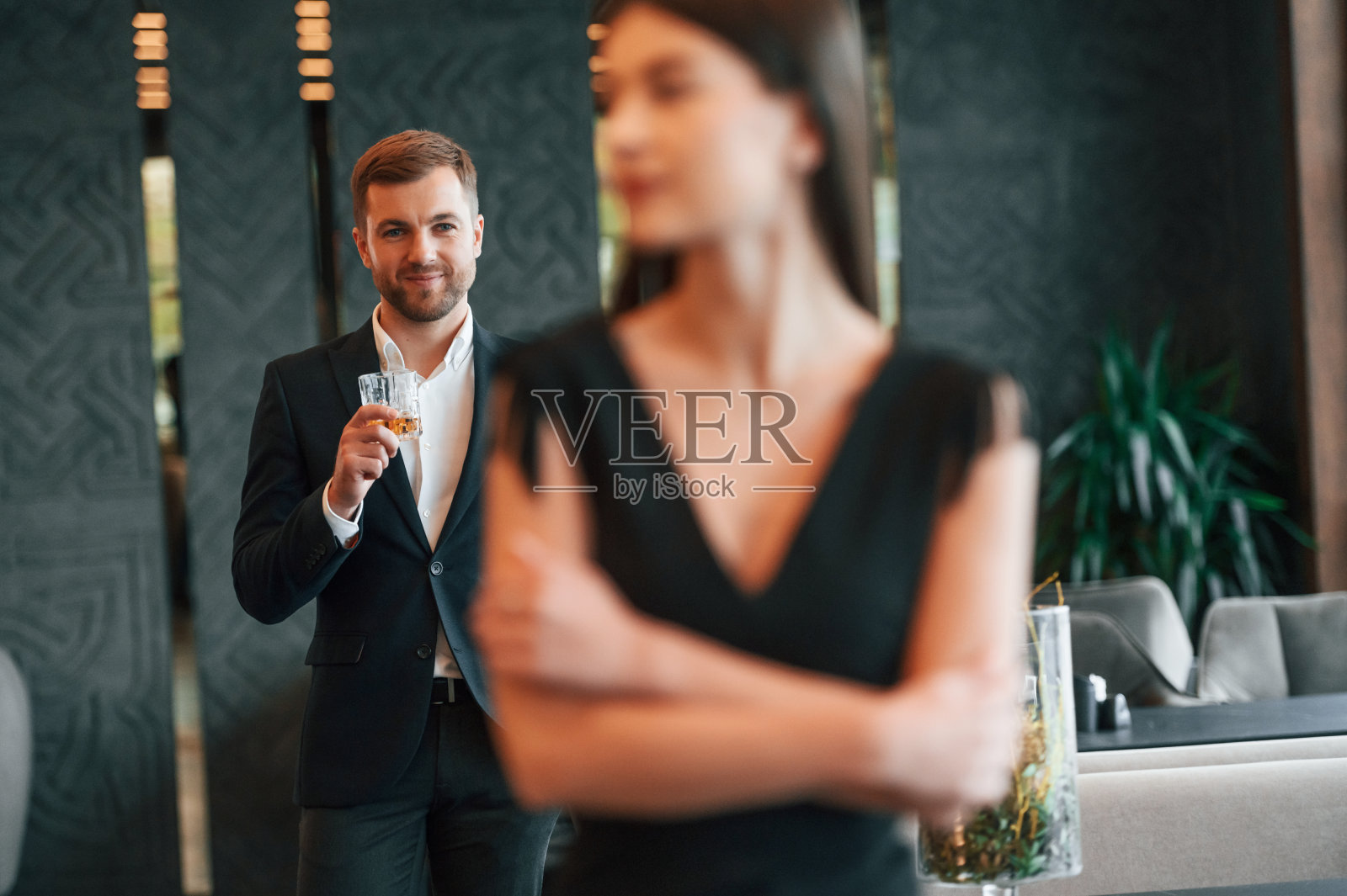 穿着黑色西装，手里拿着饮料的男人看着穿着裙子的女人照片摄影图片