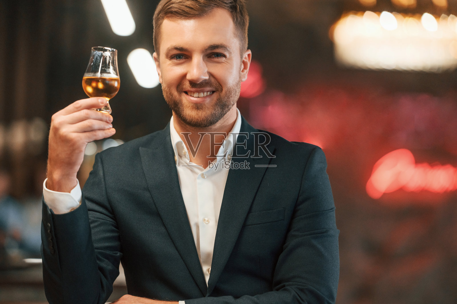 正面优雅的黑色西装男子在酒吧，品尝酒精饮料和微笑照片摄影图片