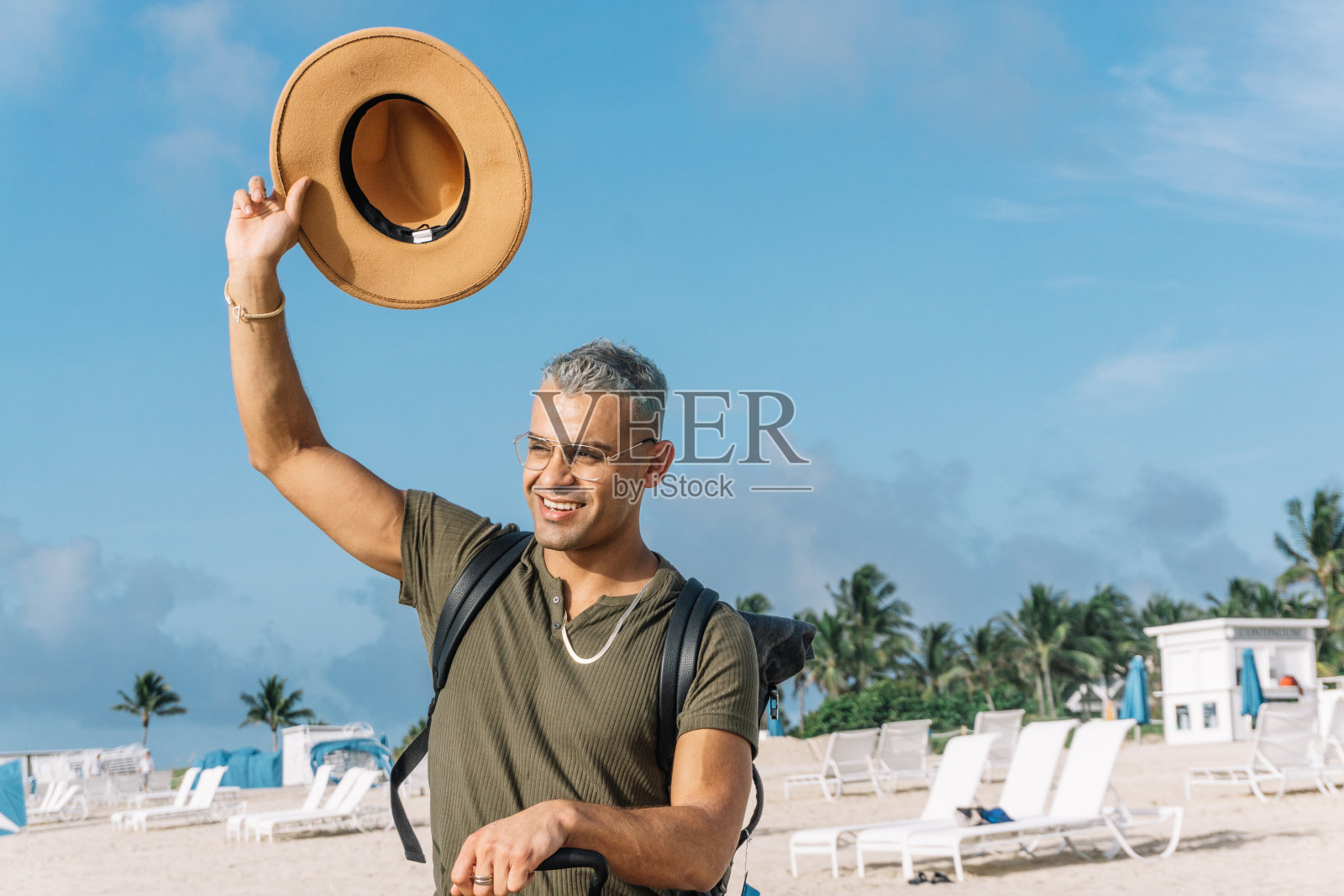 年轻人戴着牛仔帽向某人招手，坐在他提着行李的座位上。照片摄影图片