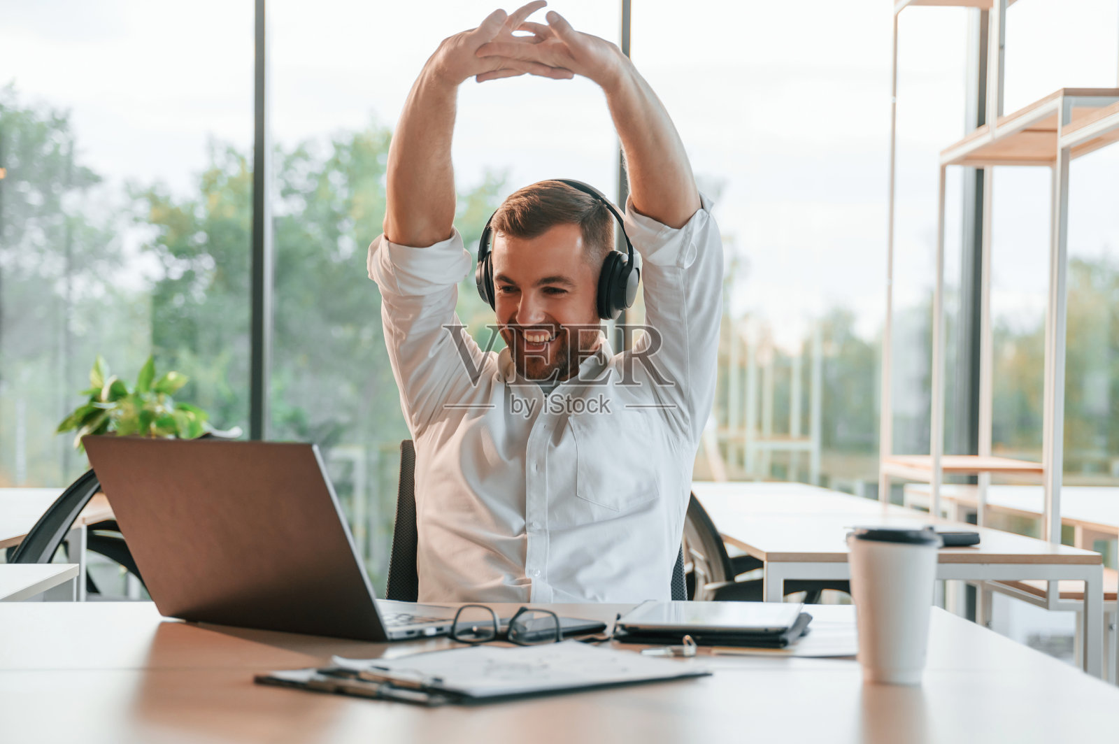 戴着耳机坐在笔记本电脑前。一个穿着正装的男人在现代化的办公室里工作照片摄影图片