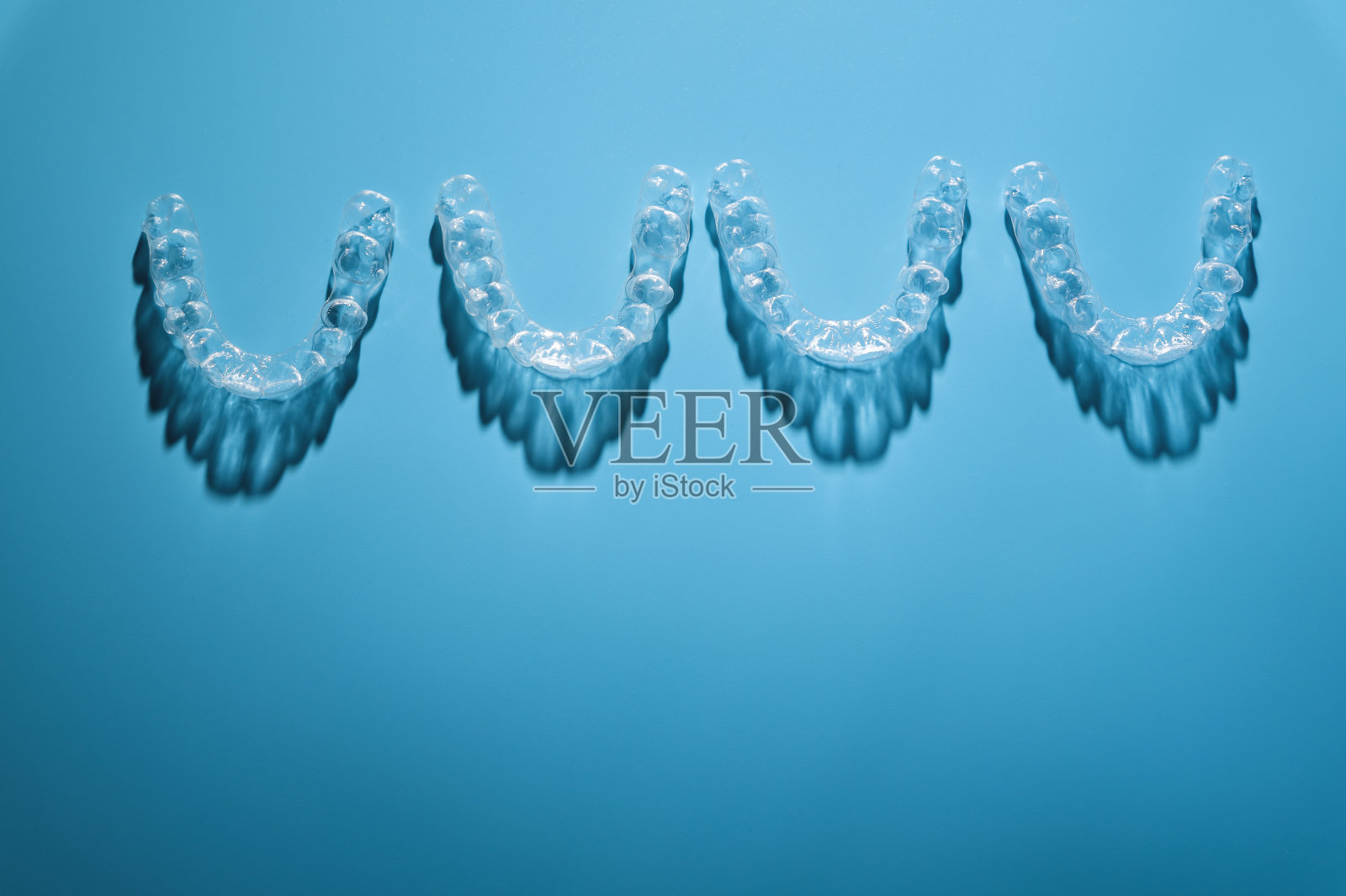 牙科诊所或正畸学背景。蓝色背景上，一排看不见的塑料新牙套，工作室用阴影拍摄照片摄影图片