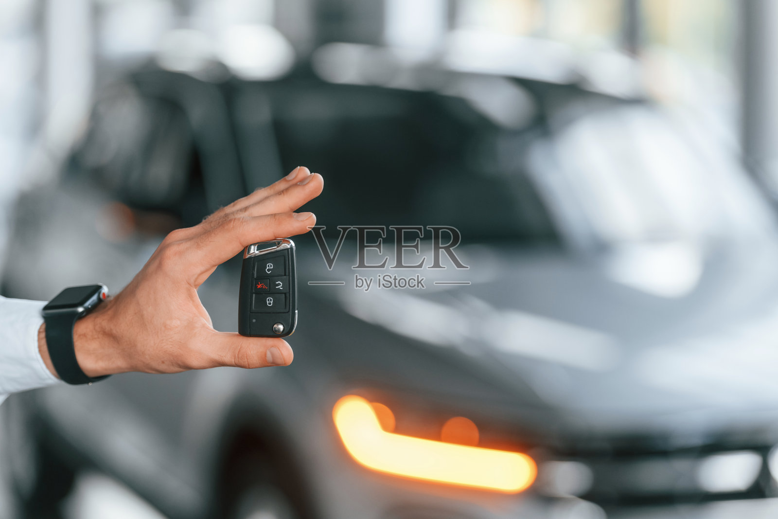 使用遥控器按键。一个穿白衣服的年轻人在汽车经销店里照片摄影图片