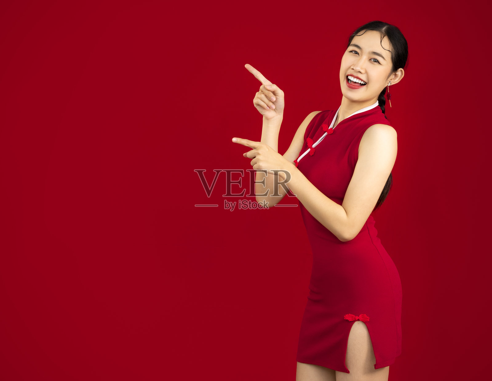 肖像亚洲妇女在红色传统中国服装摆出手指指向红色背景。春节快乐。照片摄影图片