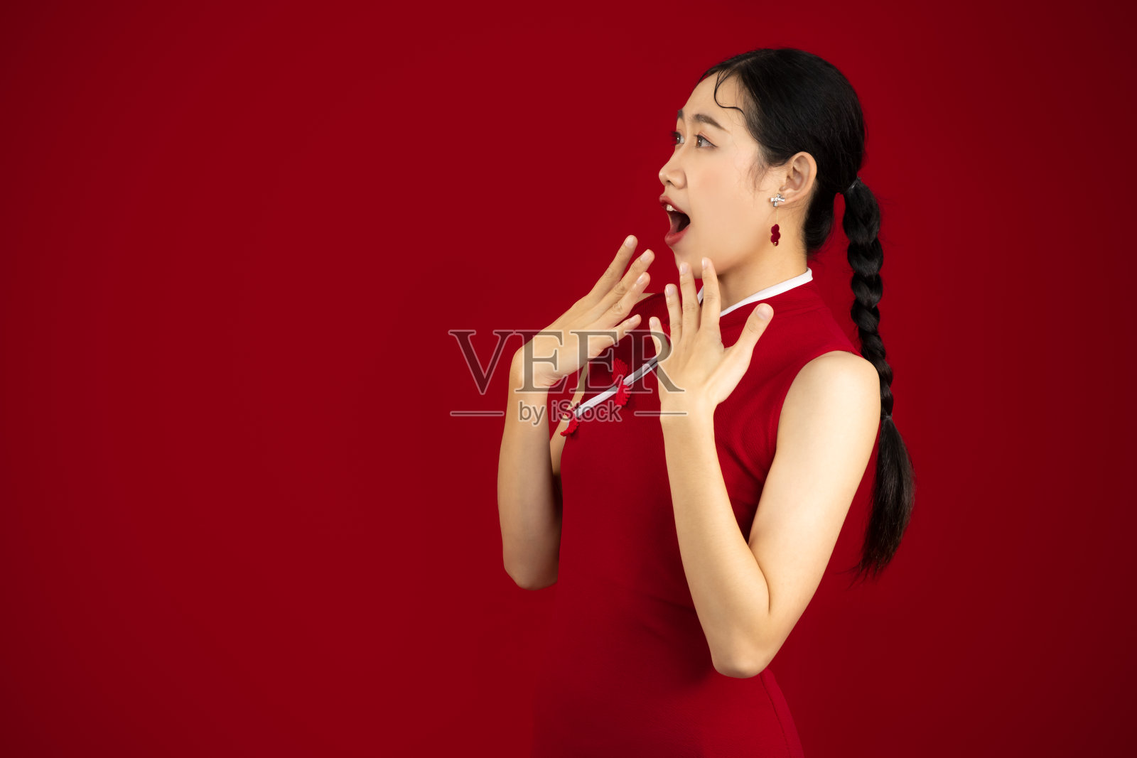 穿着红色传统中国服装的亚洲妇女在红色墙壁背景上摆出兴奋的脸。照片摄影图片