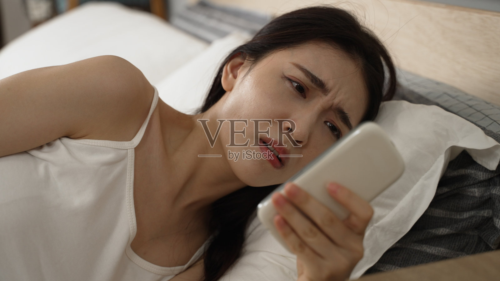 特写:一名困意十足的亚裔中国女性被手机闹钟吵醒，关机后在家里的卧室查看时间，她还在睡觉。照片摄影图片