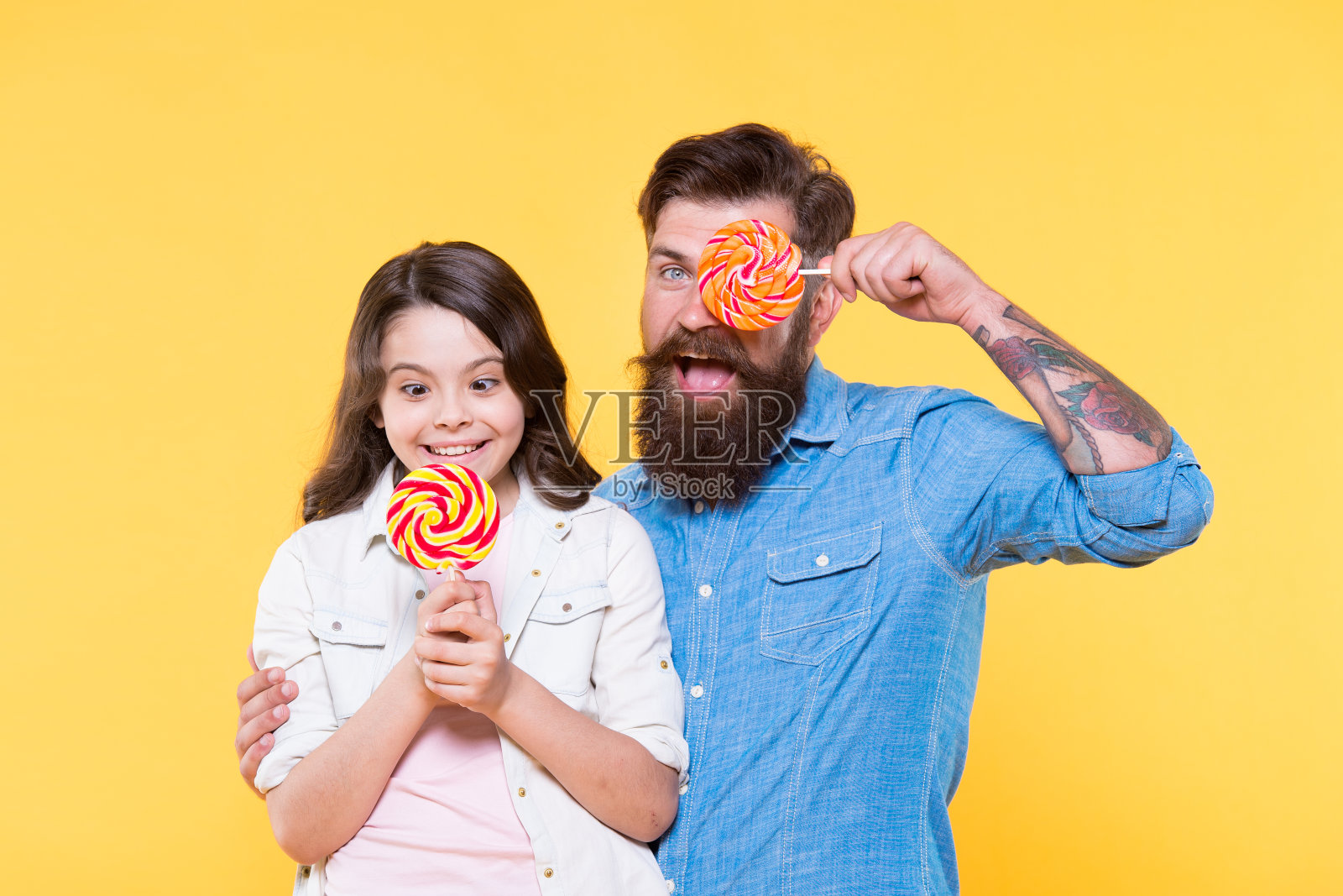 愉快的一天。爸爸和小女孩喜欢五颜六色的棒棒糖。夏天的氛围。阖家欢乐休息。卫生保健。甜蜜的童年。女儿和父亲吃糖果。留胡子的潮人是好爸爸照片摄影图片