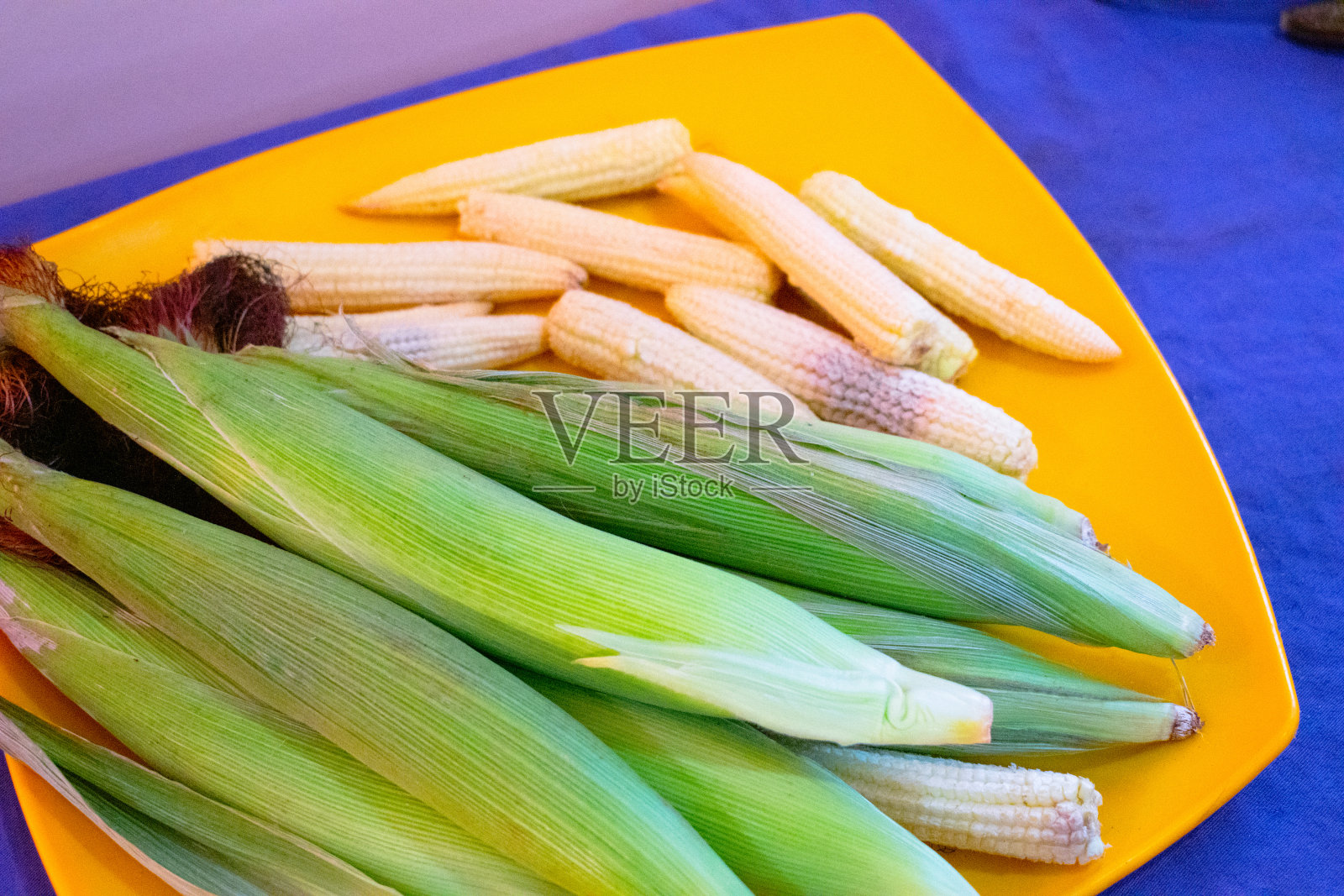 盘上一组带壳和不带壳的小玉米。特写镜头。照片摄影图片