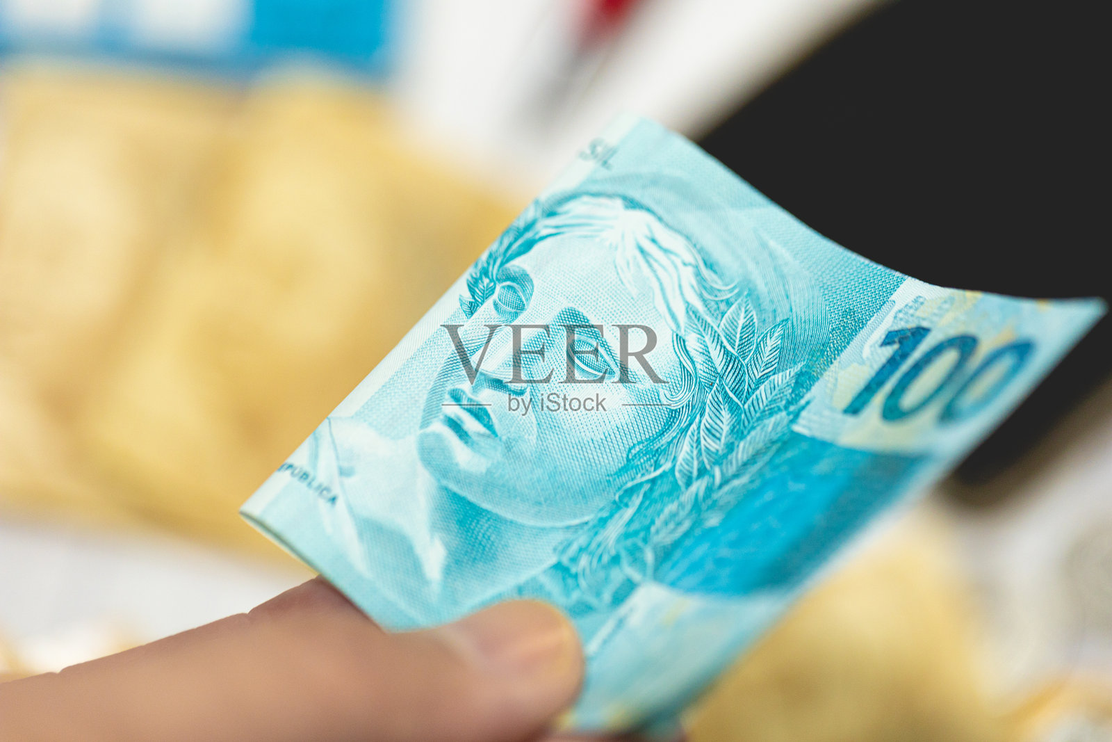 一名男子手里拿着价值100雷亚尔的巴西雷亚尔钞票。巴西经济和金融。照片摄影图片