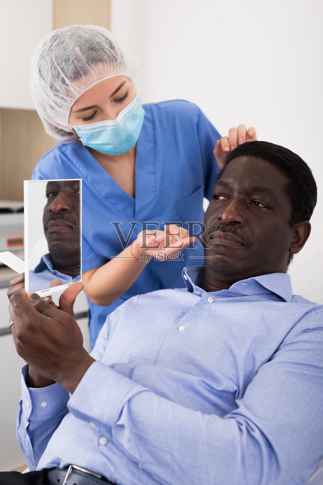 化妆师解释面部程序时，男子看着镜子照片摄影图片