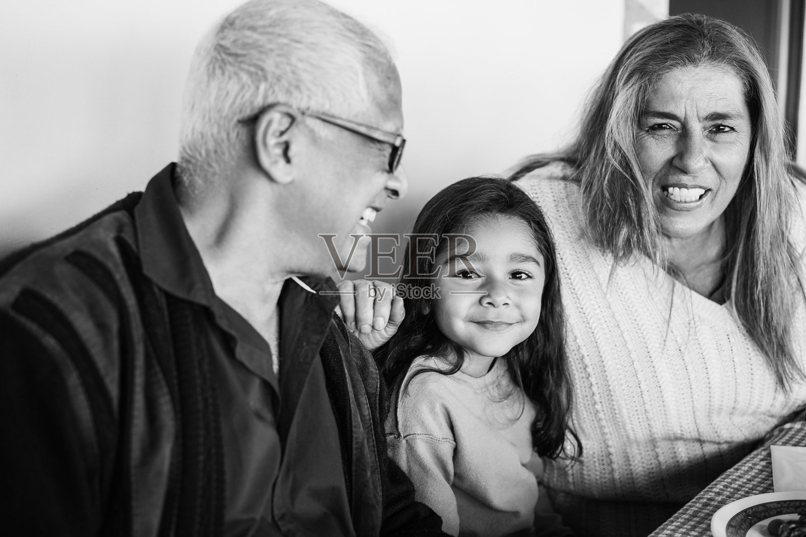 快乐的拉丁祖父母有乐趣与孙女在天井家吃饭-专注于女孩的脸-黑白编辑照片摄影图片