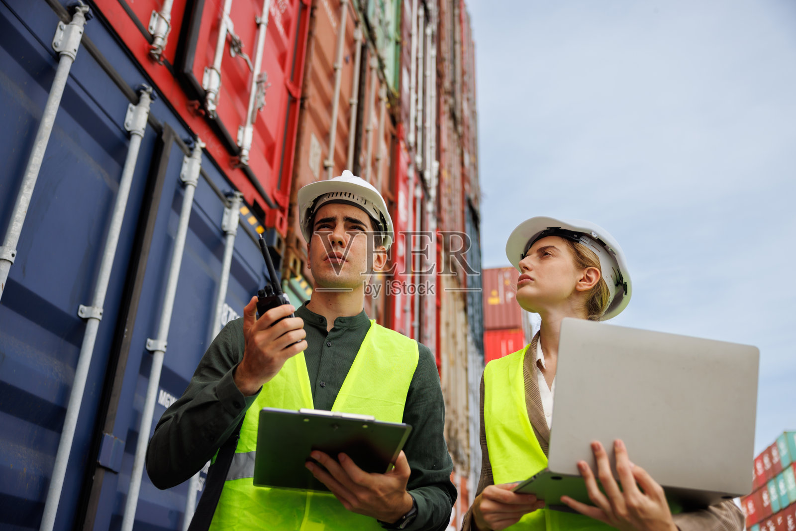在进出口集装箱船坞，男工程师和女工程师正在讨论和使用笔记本电脑。理念:运用技术控制物流与大数据分析。照片摄影图片