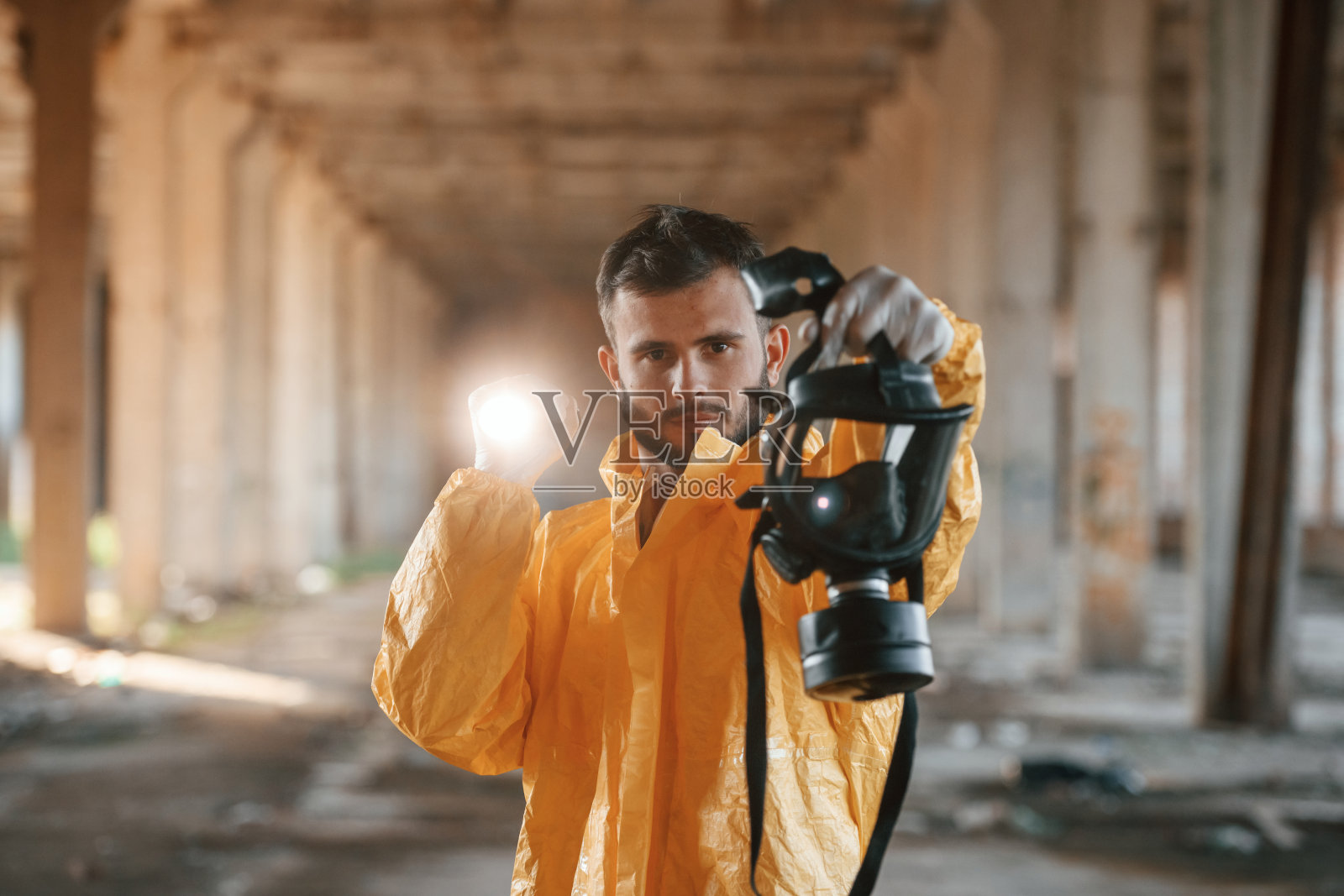 拿着呼吸器。一名穿着化学防护服的男子站在后启示性建筑的废墟中照片摄影图片