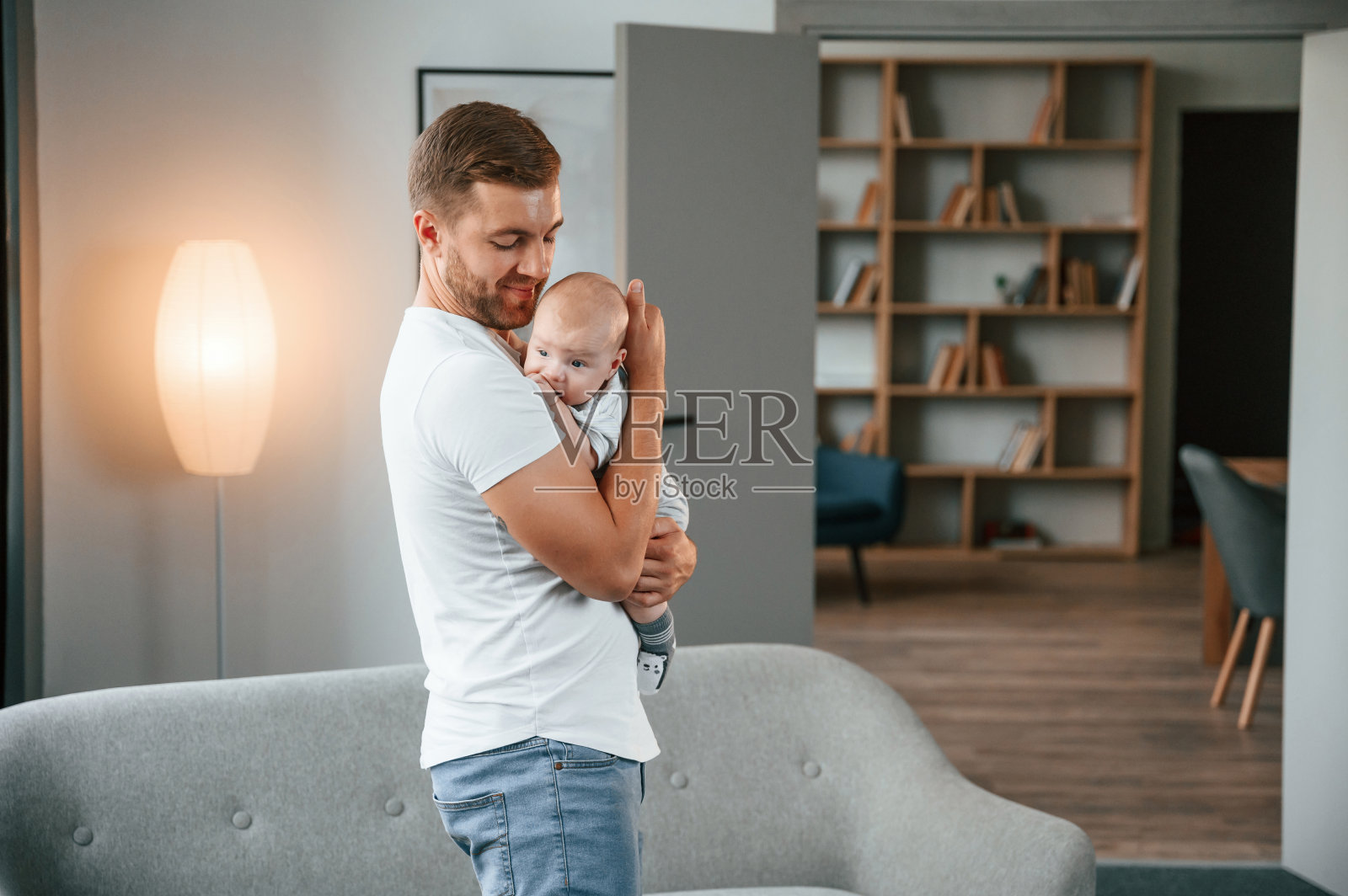 手里抱着孩子站着。父亲带着蹒跚学步的孩子在家照顾他的儿子照片摄影图片