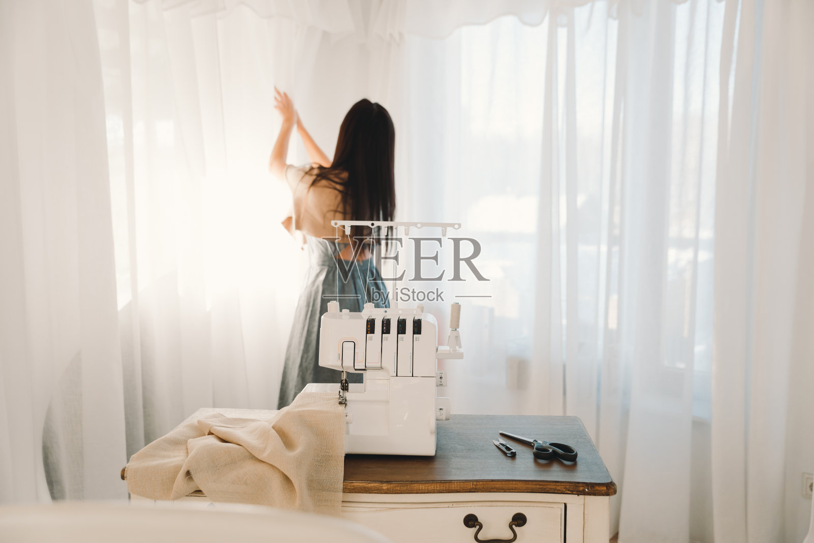 在家缝窗帘的女裁缝的工作场所。女孩拉上窗帘。照片摄影图片