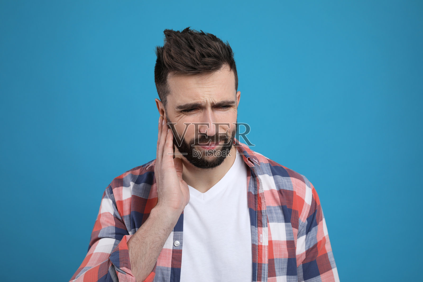 浅蓝色背景上的男子遭受耳朵疼痛照片摄影图片