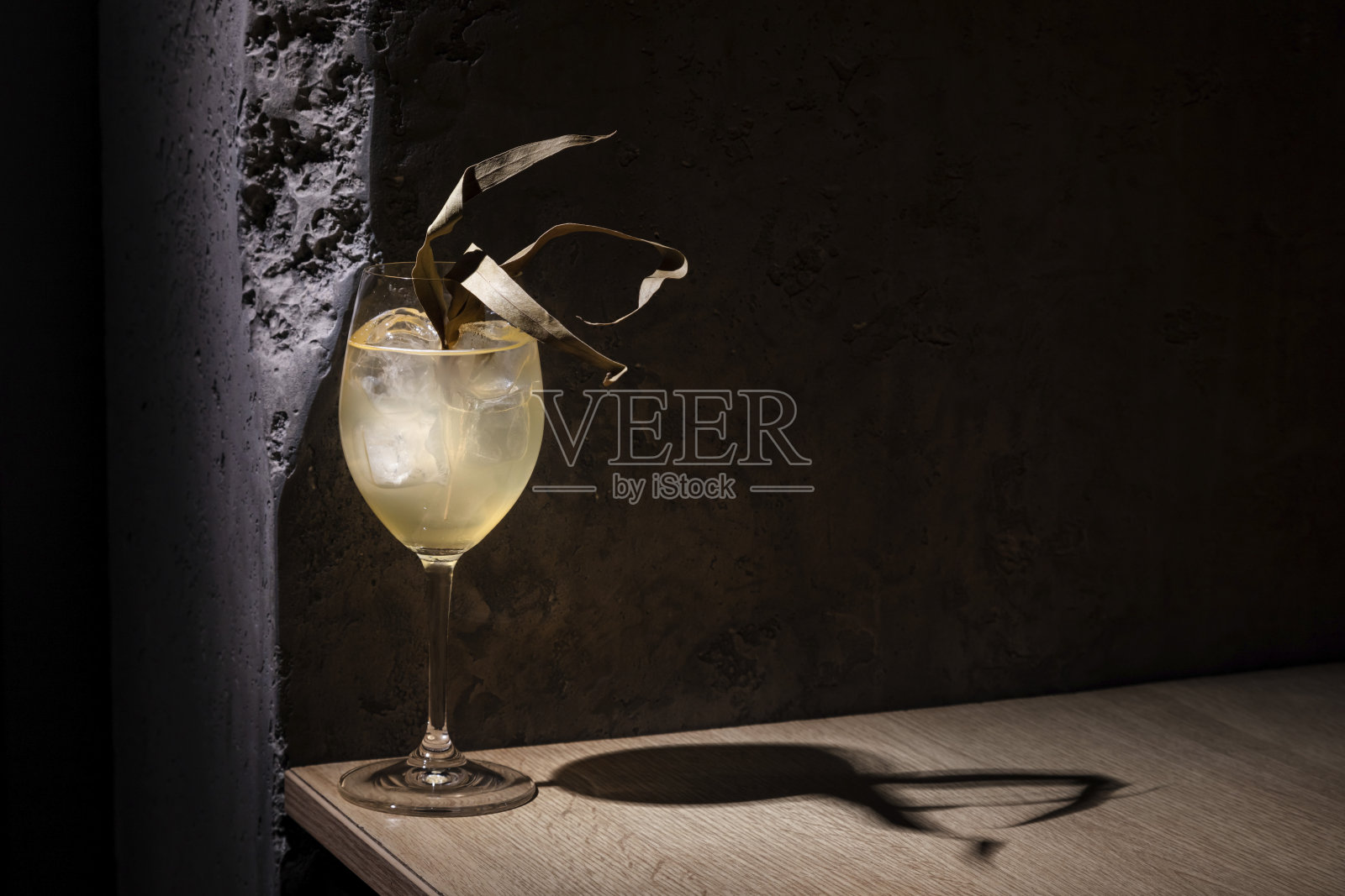 一杯鸡尾酒加冰，杯中有一根草，杯子放在桌子上，背景是一堵石墙照片摄影图片