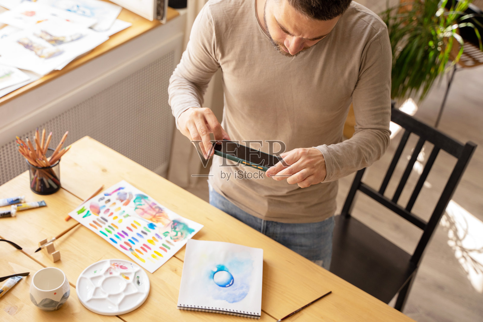 艺术家在他的工作室里。一个有创意的人为社交网络创作数字内容。年轻的艺术家通过信使发送他的作品照片。DIY概念，艺术家工作室照片摄影图片