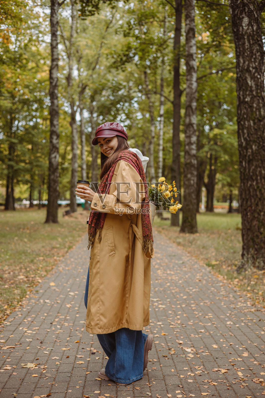 积极的年轻女子带着外卖咖啡杯在秋天的自然公园散步照片摄影图片