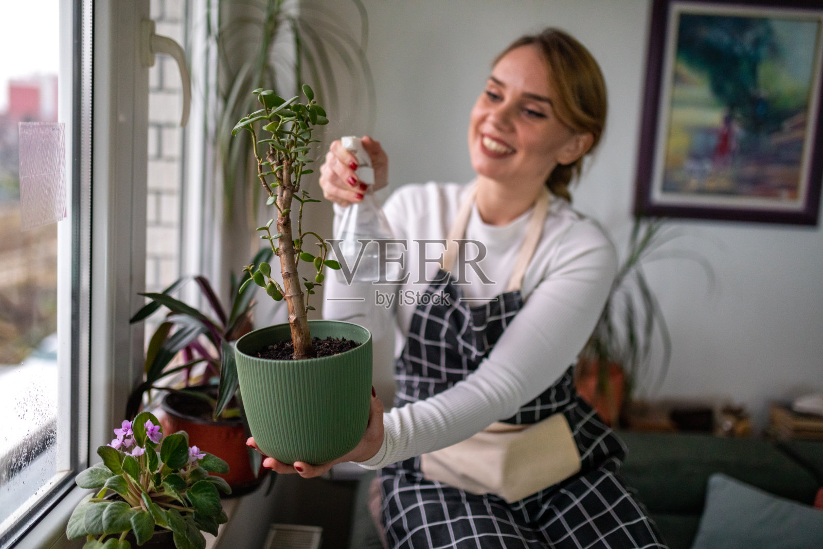 一位系着围裙的年轻女子坐在窗台上享受浇花的乐趣照片摄影图片