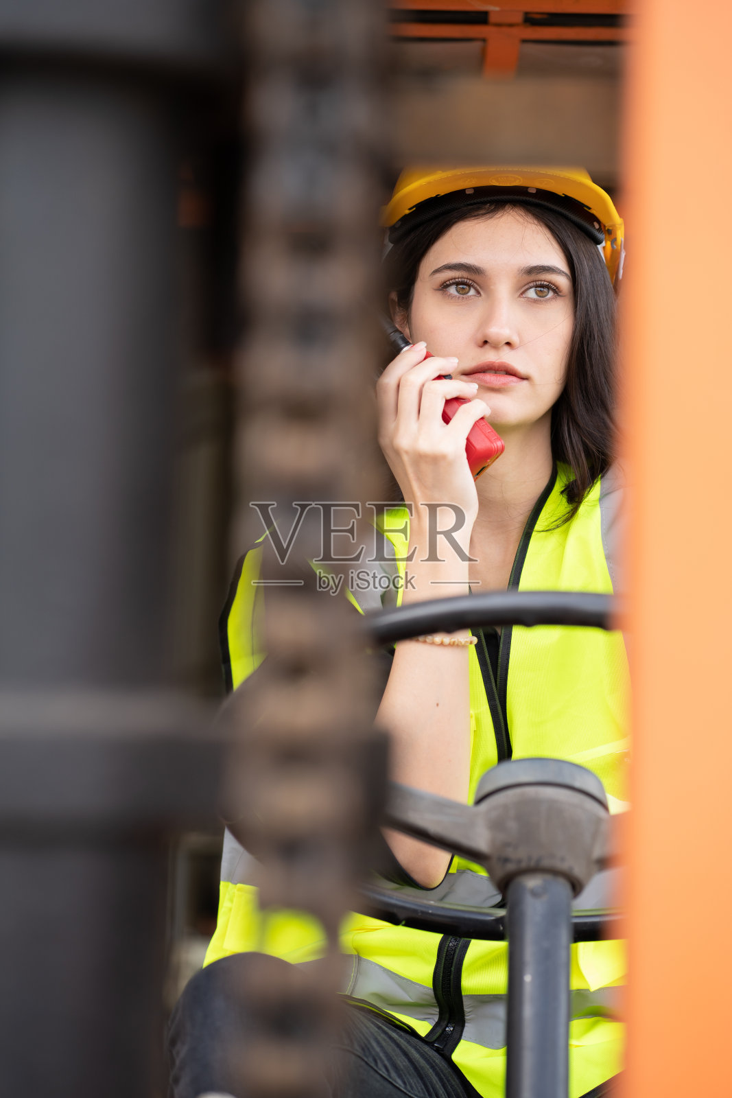 女领班在集装箱堆场驾驶叉车时使用无线电通讯。照片摄影图片