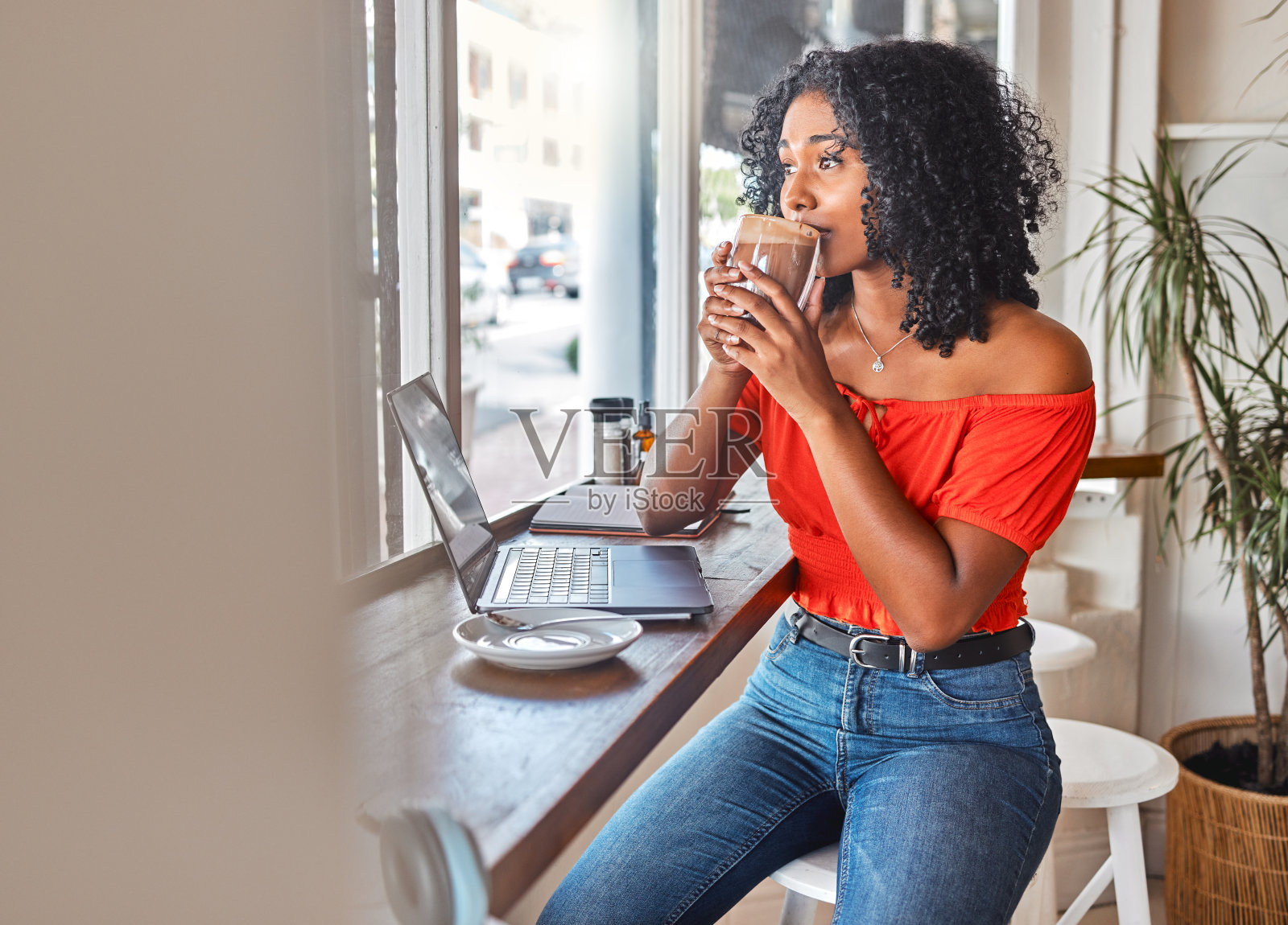 咖啡馆里，一个黑人女人一边喝着咖啡，一边看着窗外。学生在咖啡馆用笔记本电脑工作，休息一下喝热巧克力，为项目思考和头脑风暴照片摄影图片