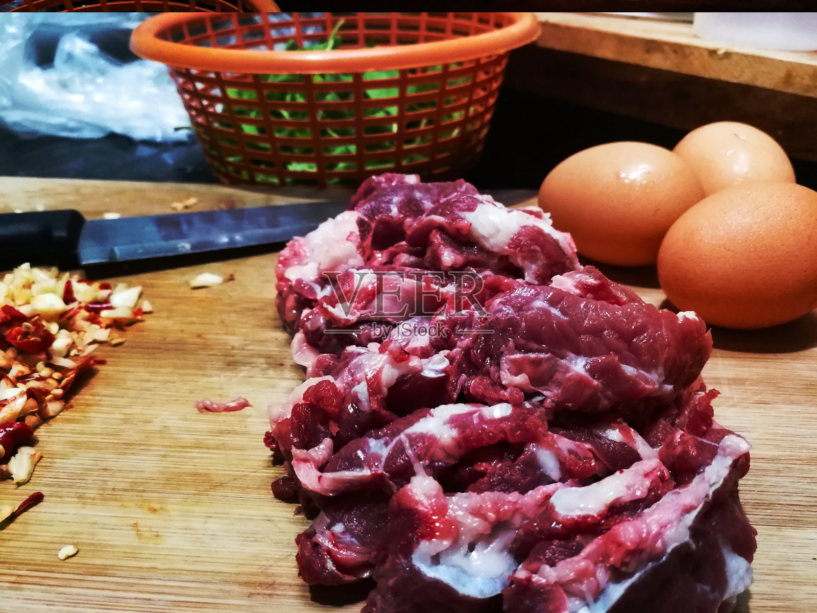 烹饪食材名称:罗勒牛肉炒蛋。切碎的新鲜辣椒和大蒜放在一个木砧板上用刀。圣罗勒叶装在橙色篮子里照片摄影图片