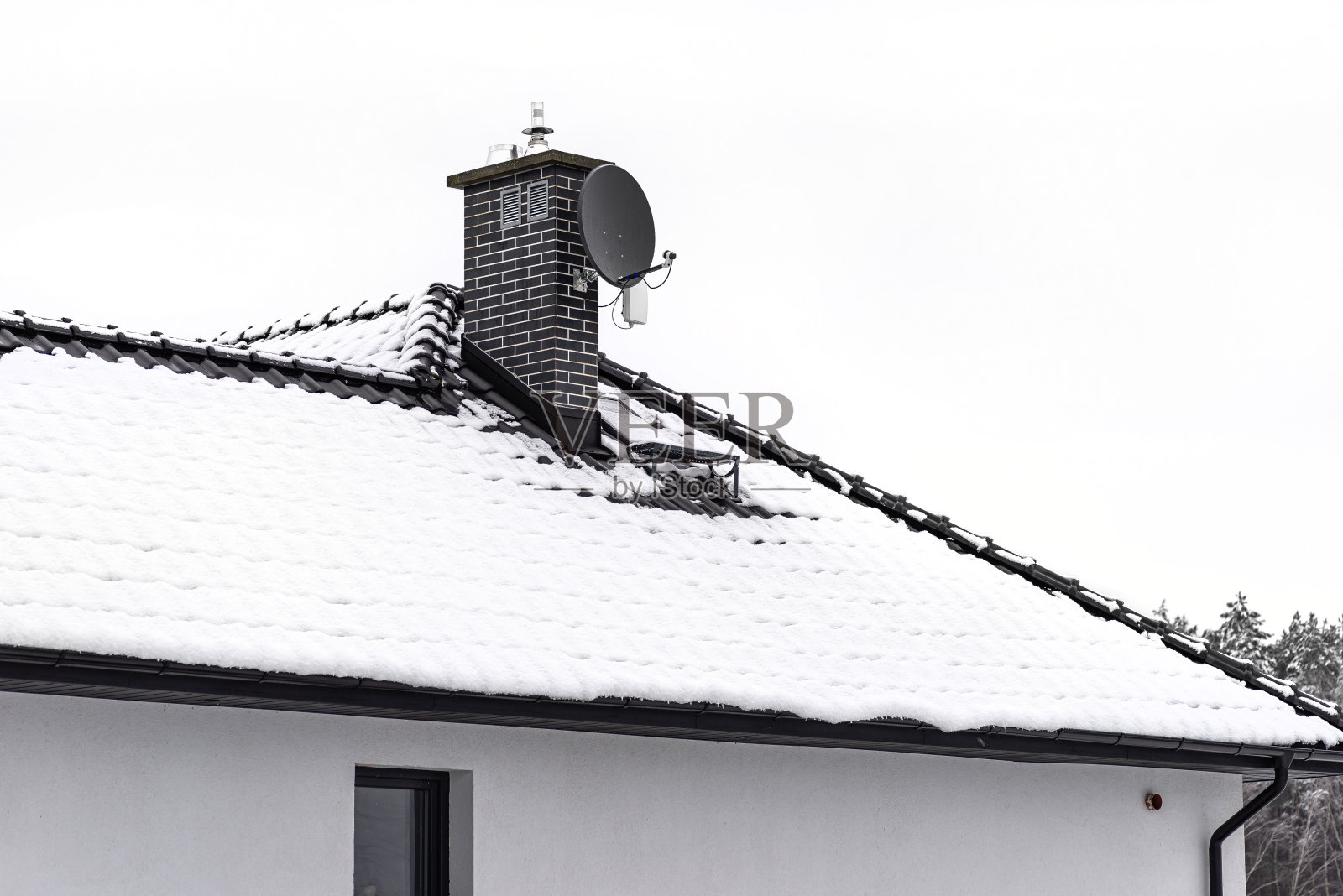 在多云的天空下，独栋住宅的屋顶覆盖着积雪，可以看到陶瓷通风壁炉和卫星天线。照片摄影图片