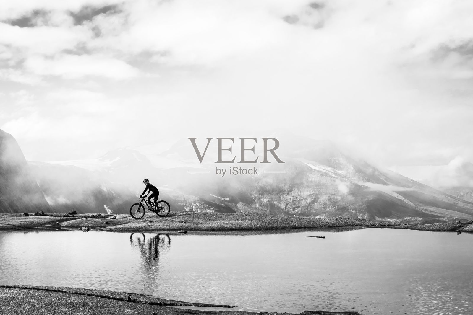 男人沿着山上的池塘骑自行车照片摄影图片