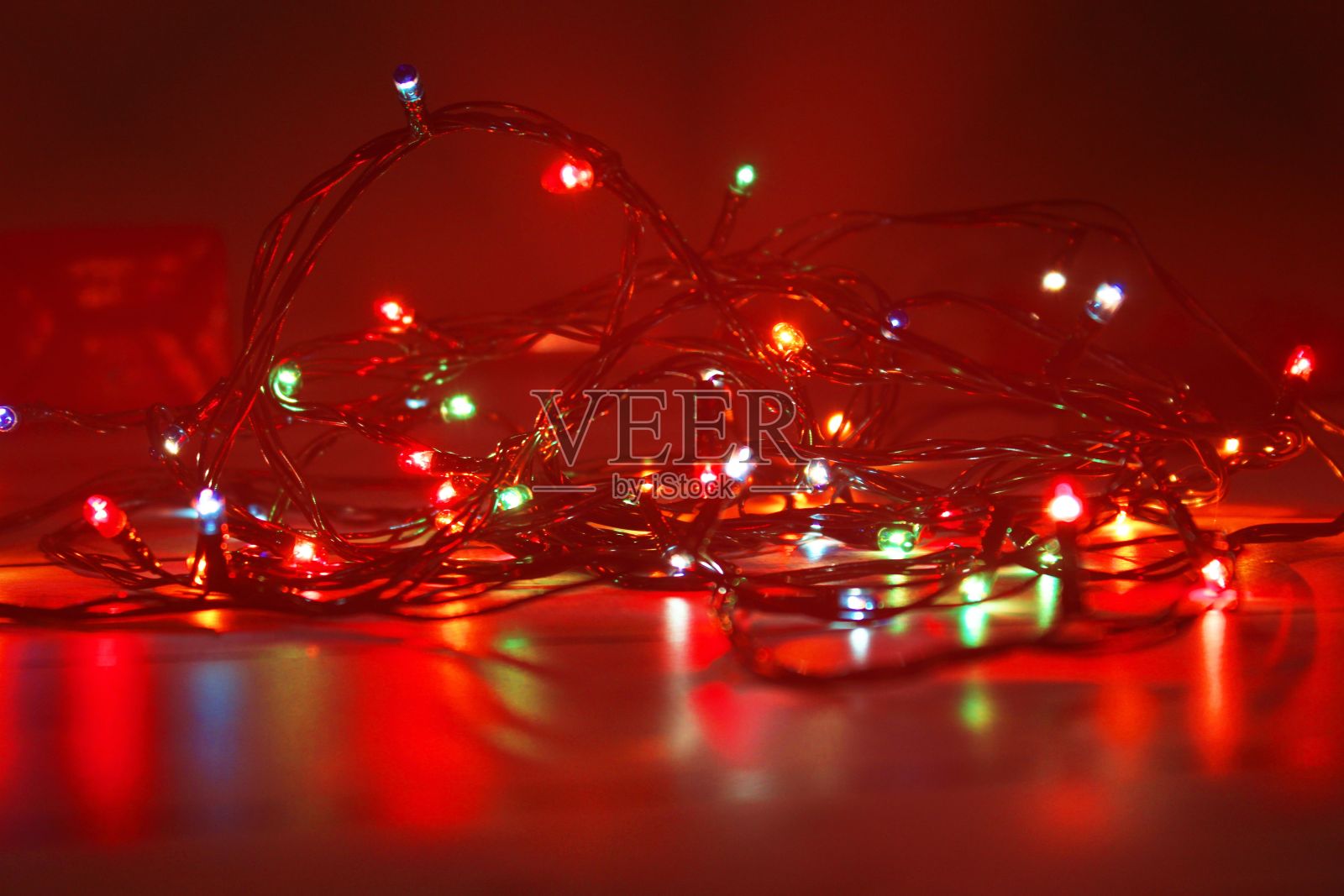 在模糊的红色背景上，彩色发光的圣诞花环的特写镜头照片摄影图片